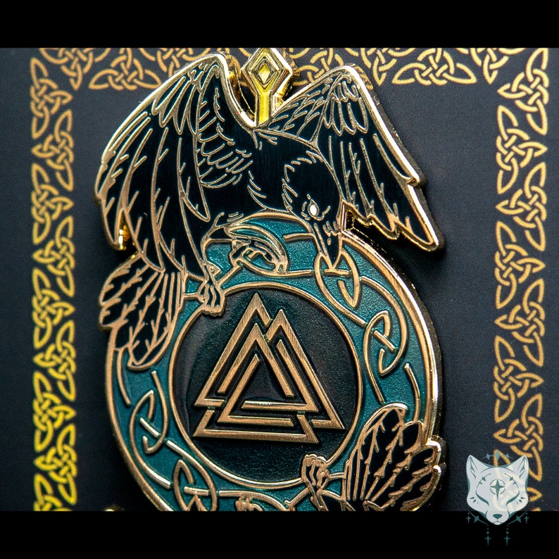 May include: A black and gold enamel pin featuring a raven perched on a circular design with a gold Valknut symbol. The raven has a green background and the Valknut is surrounded by a gold Celtic knot design.