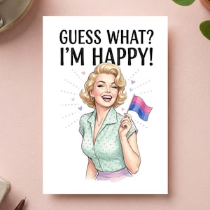 Può includere: Un biglietto d'auguri con una persona bionda in una camicia verde chiaro a pois che tiene in mano una piccola bandiera del pride bisessuale. Il testo in alto recita GUESS WHAT? I'M HAPPY! L'illustrazione include piccoli cuori viola e linee.