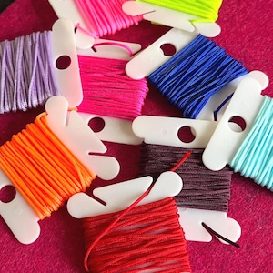 May include: Assortment of colourful embroidery floss spools in white plastic bobbins. The colours include orange, red, pink, purple, blue, green, and turquoise.