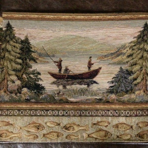 May include: Tapestry featuring a fishing scene with a boat on a lake, surrounded by trees and mountains. The bottom border has a repeating pattern of fish. The color palette includes shades of brown, green, and beige.