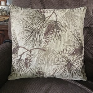 May include: A decorative throw pillow with a brown and beige pine cone and branch pattern.