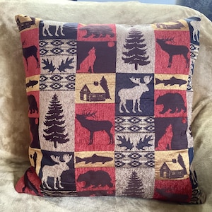 May include: A red, brown, and blue throw pillow with a patchwork design featuring various woodland creatures, including deer, moose, bears, and fish. The pillow has a rustic cabin theme.