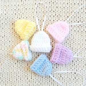 Puede incluir: Seis gorros de bebé de ganchillo en varios colores, incluyendo amarillo, rosa, blanco, azul claro y morado, con lazos de cinta blanca.