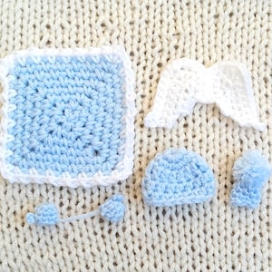 Puede incluir: Un conjunto de artículos de ganchillo hechos a mano en azul claro y blanco. El conjunto incluye un cuadrado, un par de alas de ángel, un sombrero pequeño y un pompón con una cuerda. Los artículos se muestran sobre una superficie de punto color crema.