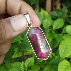 May include: A silver pendant featuring a faceted, pink and red gemstone with a geometric shape.