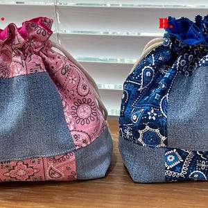 K&ouml;nnte beinhalten: Zwei Kordelzugbeutel. Einer ist rosa mit einem Paisley-Muster und Jeans-Eins&auml;tzen. Der andere ist blau mit einem Paisley-Muster und Jeans-Eins&auml;tzen. Beide Taschen haben einen beigen Kordelzugverschluss.