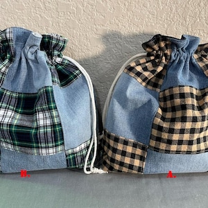 Peut inclure: Deux sacs à cordon de serrage avec un motif patchwork. Les sacs combinent du denim avec du tissu à carreaux vert, noir et beige. Chaque sac a une fermeture à cordon blanche. Les sacs sont étiquetés avec les lettres "A" et "B".
