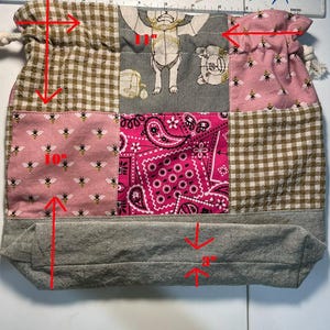 May include: A patchwork drawstring bag with various fabrics. The bag includes pink fabric with bees, brown gingham, pink paisley, and grey fabric. The bag is approx. 25 cm tall, 28 cm wide, and 7.6 cm deep.