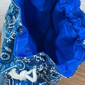 K&ouml;nnte beinhalten: Ein blauer Kordelzugbeutel mit einem Paisley-Muster in Blau- und Wei&szlig;t&ouml;nen. Der Innenraum ist einfarbig hellblau. Die Tasche ist aus Stoff und hat einen wei&szlig;en Kordelzugverschluss.