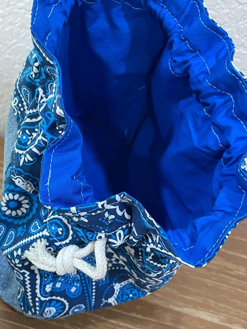 K&ouml;nnte beinhalten: Ein blauer Kordelzugbeutel mit einem Paisley-Muster in Blau- und Wei&szlig;t&ouml;nen. Der Innenraum ist einfarbig hellblau. Die Tasche ist aus Stoff und hat einen wei&szlig;en Kordelzugverschluss.