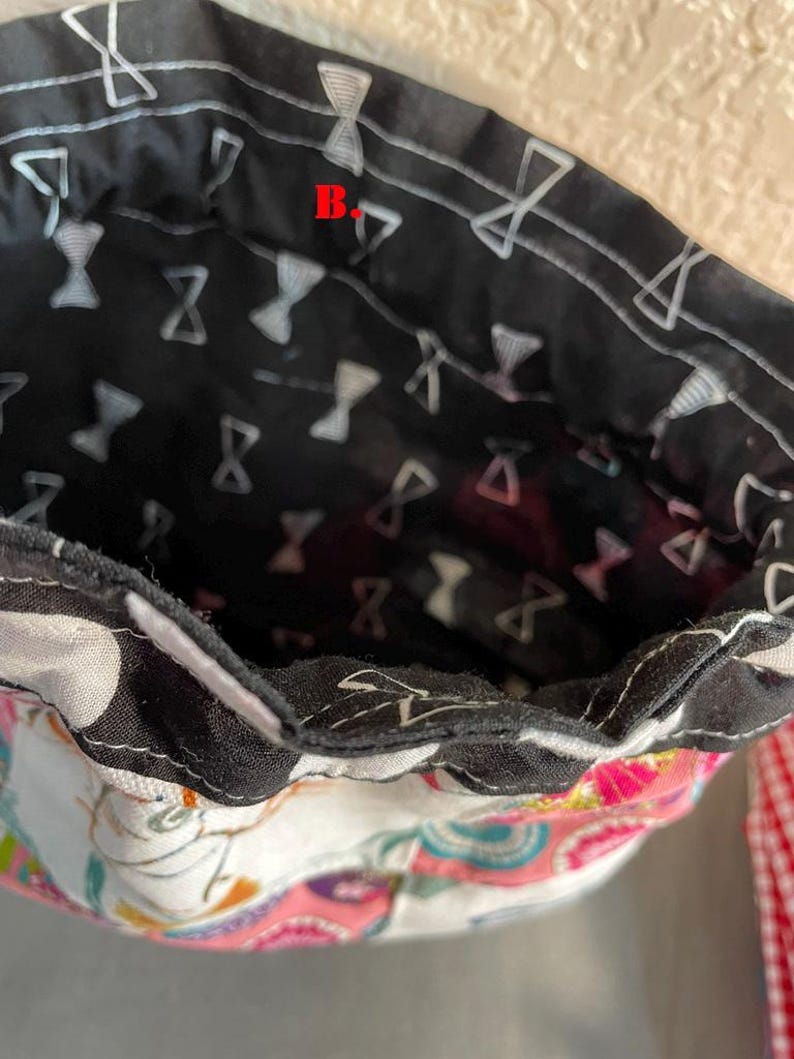 Pu&ograve; includere: Primo piano dell'interno di una borsa in tessuto. La fodera interna &egrave; nera con un motivo a farfalla bianco. Il tessuto esterno presenta un colorato design floreale e paisley. &Egrave; visibile una cinghia a scacchi rossi e bianchi.