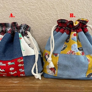 May include: Two drawstring bags with patchwork designs. One bag features a red panel with cat illustrations, while the other has a yellow panel with Japanese-inspired motifs. Both bags have denim and patterned fabric panels, with a plaid fabric at the top.