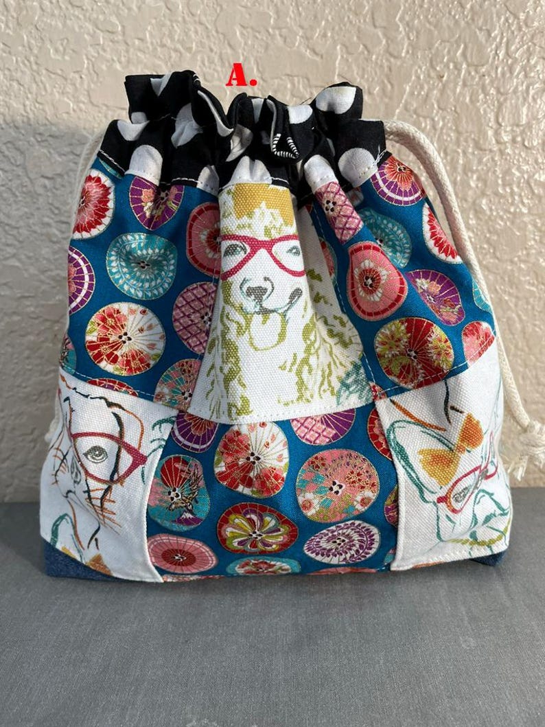 Pu&ograve; includere: Una borsa con coulisse con un design patchwork. La borsa presenta uno sfondo blu con motivi circolari colorati, pannelli bianchi con occhiali e un lama con gli occhiali. La parte superiore &egrave; nera con pois bianchi.
