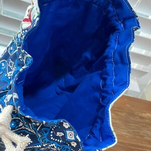 May include: A blue drawstring bag with a white rope closure. The bag's exterior features a paisley pattern in shades of blue and white. The interior is a vibrant blue, and the bag is held open.