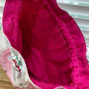 May include: Open view of a handmade tote bag with a bright pink interior. The bag's exterior features a patchwork design with floral and paisley patterns in shades of pink, white, and blue. The interior lining is a solid, vibrant pink fabric.