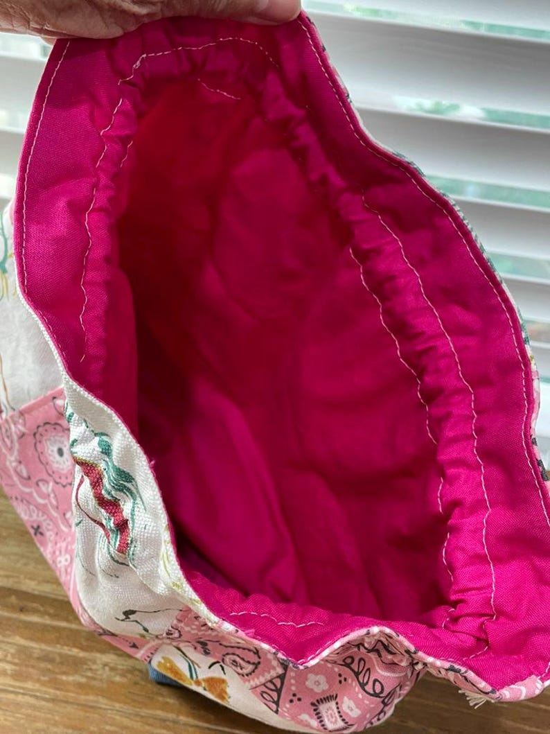 May include: Open view of a handmade tote bag with a bright pink interior. The bag's exterior features a patchwork design with floral and paisley patterns in shades of pink, white, and blue. The interior lining is a solid, vibrant pink fabric.