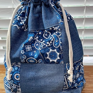 Peut inclure: Un sac en jean à cordon de serrage avec un motif patchwork. Le sac présente différentes nuances de denim bleu et un motif cachemire bleu et blanc. Un cordon de serrage en corde blanche ferme le sac.