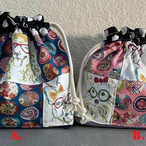 May include: Two drawstring bags with a patchwork design. One bag features a blue background with colorful circles and dog illustrations wearing glasses. The other bag has a pink background with similar patterns and dog illustrations. Both bags have a black and white polka dot trim.