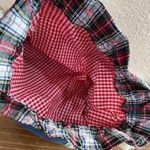 May include: A drawstring bag with a red and white gingham interior. The bag's exterior features a plaid pattern in red, green, black, and white. The bag is made of fabric and has a denim base.