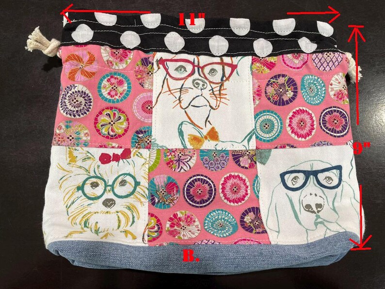Pu&ograve; includere: Una borsa a coulisse patchwork, larga 28 cm e alta 23 cm, con illustrazioni di cani con gli occhiali. La borsa ha una base in denim, un motivo floreale rosa e una parte superiore a pois bianchi e neri.