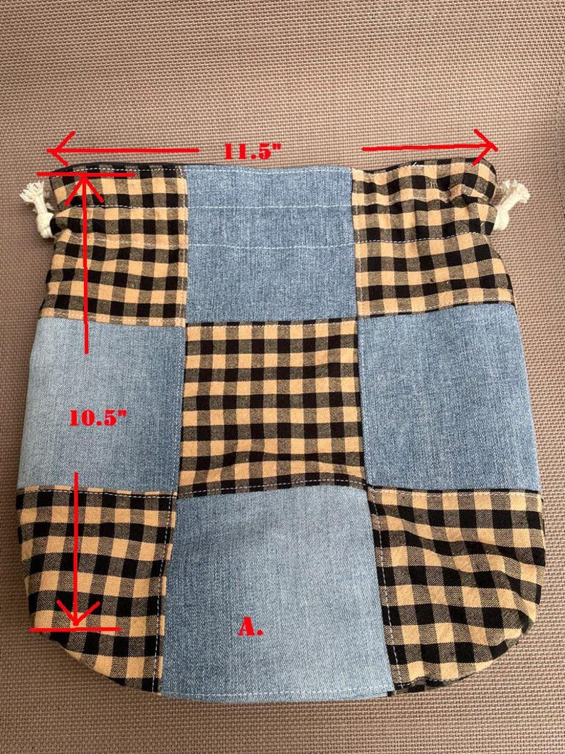 May include: Patchwork tote bag with a denim and black and tan plaid design. The bag is 11.5 inches wide and 10.5 inches tall. The bag has a drawstring closure with white tassels on each side.
