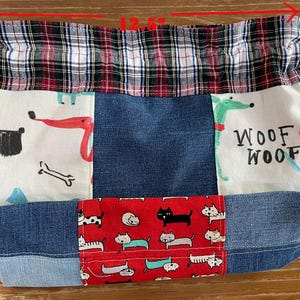 May include: A patchwork tote bag, 12.5 inches wide and 9.5 inches tall, featuring denim, plaid, and patterned fabrics. The bag has a drawstring closure and depicts dogs and cats. The top is plaid, and the bottom is denim.