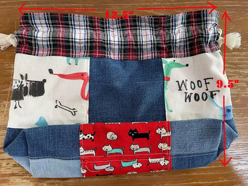 May include: A patchwork tote bag, 12.5 inches wide and 9.5 inches tall, featuring denim, plaid, and patterned fabrics. The bag has a drawstring closure and depicts dogs and cats. The top is plaid, and the bottom is denim.