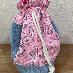 K&ouml;nnte beinhalten: Ein Kordelzugbeutel mit Jeans-Basis und einem rosa Paisley-Muster. Der Beutel hat einen wei&szlig;en Kordelzugverschluss und eine leuchtend rosa Einfassung. Der Beutel ist f&uuml;r kleine Gegenst&auml;nde konzipiert.