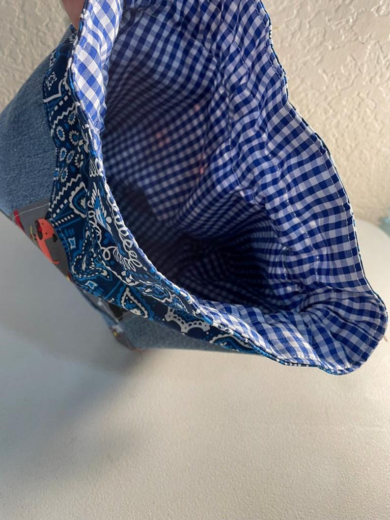 Pode incluir: Uma bolsa de ganga com forro xadrez azul e branco. A bolsa apresenta uma borda com padr&atilde;o paisley azul. A bolsa est&aacute; aberta, revelando o interior. A bolsa &eacute; feita de tecido.