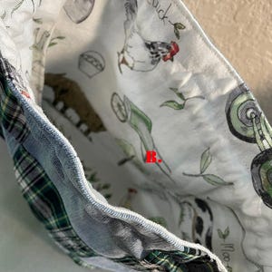 May include: A fabric bag with a patchwork design. The exterior features denim and green plaid fabric. The interior lining is white with a farm animal print, including a chicken, cow, and pig. The word "Chick" is visible.