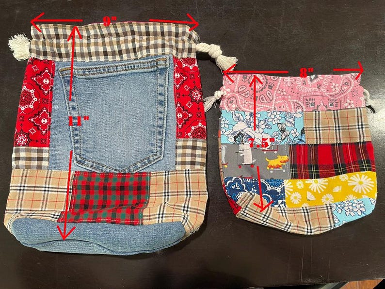 May include: Two drawstring bags. The larger bag is 9 inches wide and 11 inches tall, featuring a denim pocket and patchwork of red paisley, plaid, and denim fabrics. The smaller bag is 8 inches wide, with a patchwork design of pink paisley, floral, and plaid patterns.