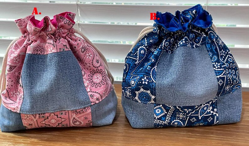 K&ouml;nnte beinhalten: Zwei Kordelzugbeutel. Einer ist rosa mit einem Paisley-Muster und Jeans-Eins&auml;tzen. Der andere ist blau mit einem Paisley-Muster und Jeans-Eins&auml;tzen. Beide Taschen haben einen beigen Kordelzugverschluss.
