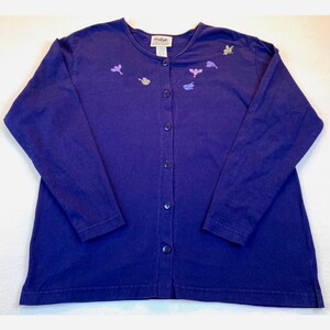 May include: A long-sleeved, button-down cardigan in a deep purple hue. The cardigan features embroidered bird designs in shades of purple, pink, and yellow. The garment has a classic, relaxed fit and is made of a soft fabric.