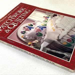 May include: A hardcover book titled Better Homes and Gardens New Patchwork & Quilting Book. The dark red cover features a white border and a central photograph of a bed decorated with floral-patterned quilts and pillows with tulip motifs.