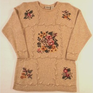 May include: A beige knitted sweater with a cable knit design and floral embroidery. The sweater features four floral motifs in shades of pink, yellow, green, and red.