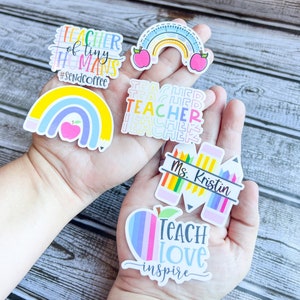 Puede incluir: Un conjunto de cinco pegatinas de profesor coloridas con varios dise&ntilde;os. Las pegatinas presentan arco&iacute;ris, manzanas, l&aacute;pices y el texto "Teacher of tiny humans #SendCoffee", "Teacher", "Ms. Kristin" y "Teach Love Inspire".