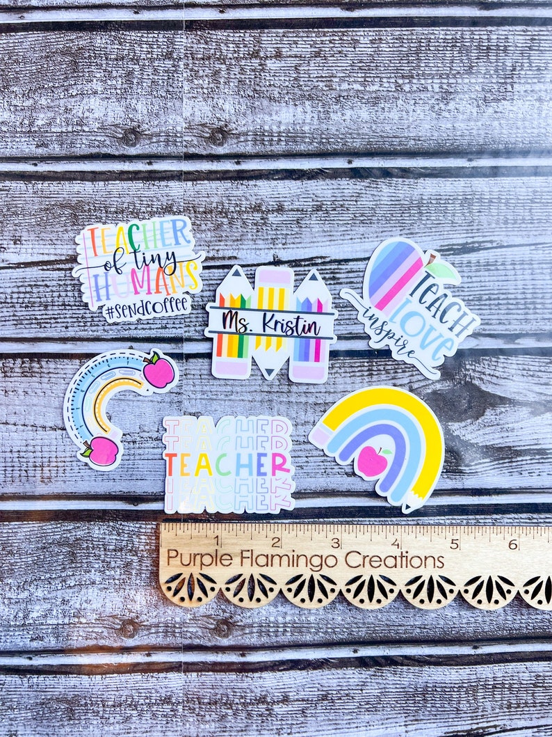 Puede incluir: Un conjunto de cinco pegatinas con tem&aacute;tica de profesor con dise&ntilde;os coloridos. Las pegatinas presentan frases como "Teacher of Tiny Humans #SendCoffee", "Teach Love Inspire" y "Teacher" repetido en un patr&oacute;n de arco&iacute;ris. Tambi&eacute;n hay una pegatina con un arco&iacute;ris y una manzana, y una pegatina con una fila de l&aacute;pices de colores y el texto "Ms. Kristin".