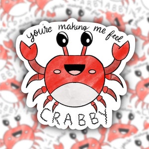 May include: A red watercolor crab sticker with the text "you're making me feel crabby". The crab has large black eyes, a smiling mouth, and is waving a claw. The sticker is white with a die-cut edge.