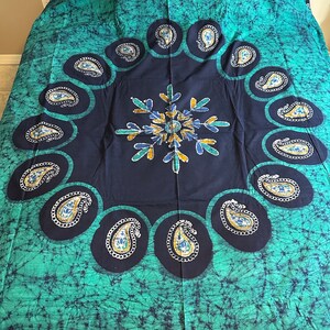 May include: A green and black batik bedspread with a circular paisley pattern. The center of the pattern features a stylized flower with blue, green, and gold accents.