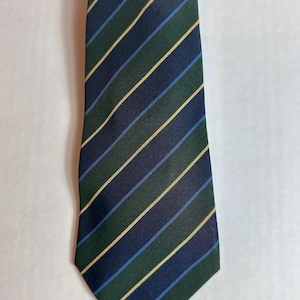 Könnte beinhalten: Eine Krawatte mit diagonalen Streifen. Sie hat abwechselnde Streifen in Dunkelgrün, Marineblau, Hellblau und Gold. Die Krawatte ist aus glattem Stoff gefertigt und eignet sich für formelle oder geschäftliche Anlässe.