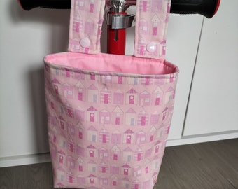 May include: Pink fabric bag with a pattern of small houses, attached to a scooter handlebar with two straps and white buttons.