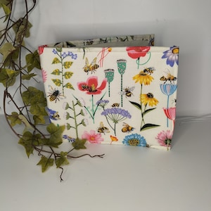 May include: A white fabric storage box with a colourful floral and bee print. The print features pink, red, yellow, blue, and green flowers, as well as bees and butterflies.