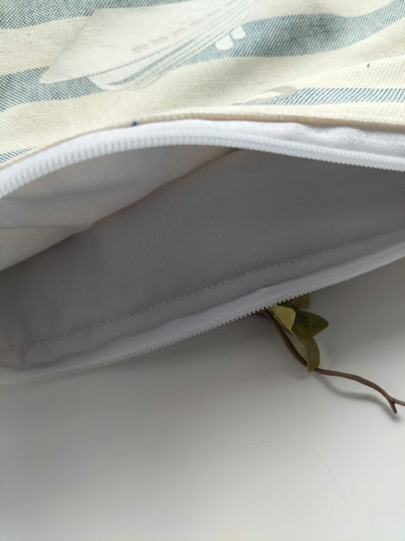 May include: A white zippered pouch with a blue and white striped fabric exterior. The pouch is open and the inside is white.