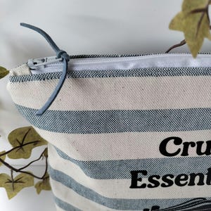 May include: A white and blue striped canvas zippered pouch with a black graphic of a cruise ship and the text "Cruise Essentials".