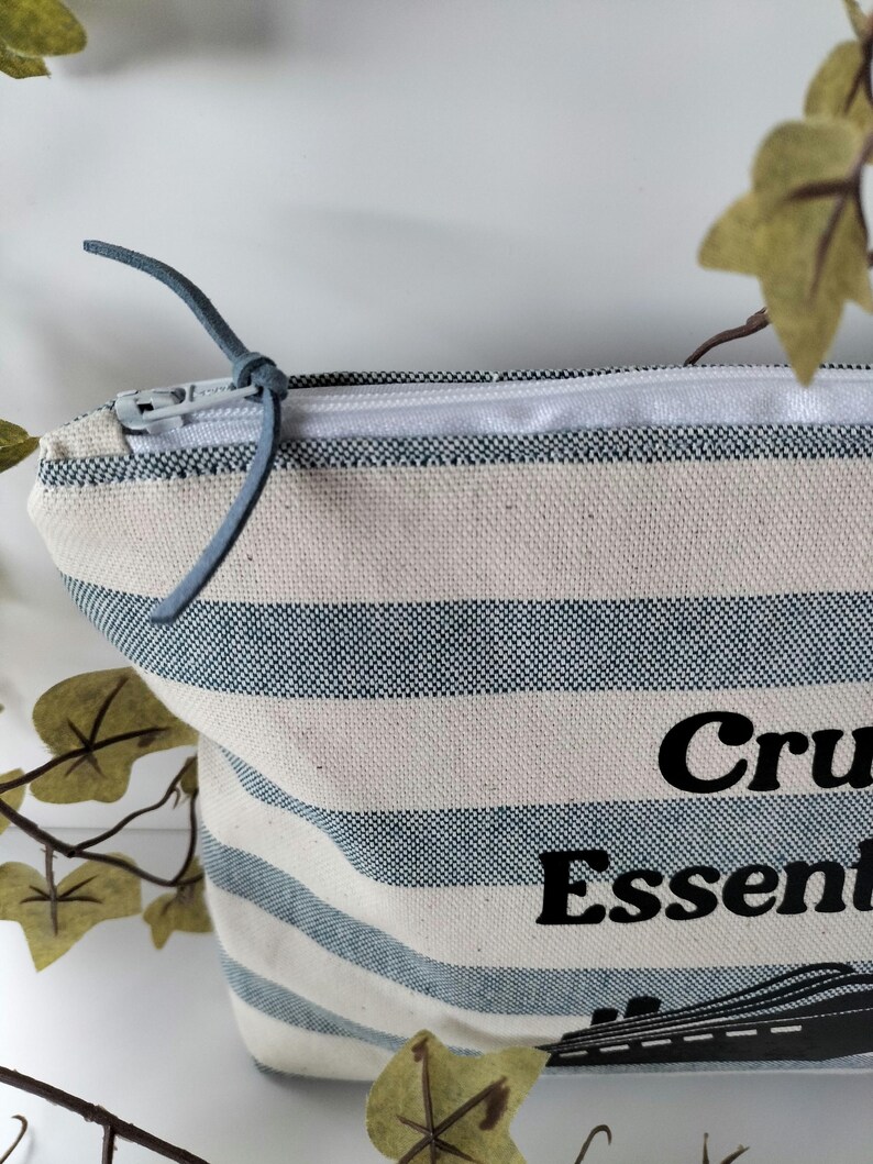 May include: A white and blue striped canvas zippered pouch with a black graphic of a cruise ship and the text "Cruise Essentials".