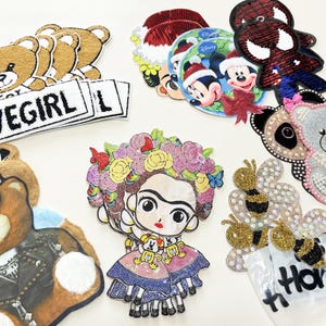 Peut inclure: Une collection de patchs brodés et à paillettes assortis présentant divers motifs, notamment des ours en peluche, des personnages de dessins animés comme Mickey et Spider-Man, une figure couronnée de fleurs, des abeilles et des textes LOVEGIRL et Honey.