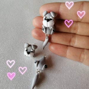 May include: Two gray miniature schnauzer dog figurines with black eyes and noses. Each figurine has a dangling tail and is attached to a silver jump ring.