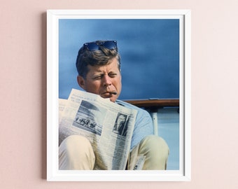 May include: A black and white photo of a man wearing sunglasses and a white shirt, sitting on a boat and reading a newspaper. The newspaper headline reads "Milwaukee Journal, Wisconsin's Afternoon Newspaper, Nov. 19, 1963".