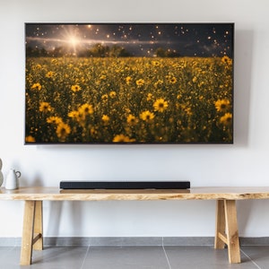 May include: A flat screen television mounted on a white wall above a wooden entertainment unit with a soundbar. The television is displaying a field of yellow flowers with a bright sun shining in the background.