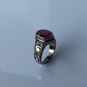 Puede incluir: Un anillo de plata con un diseño adornado y una piedra preciosa roja.